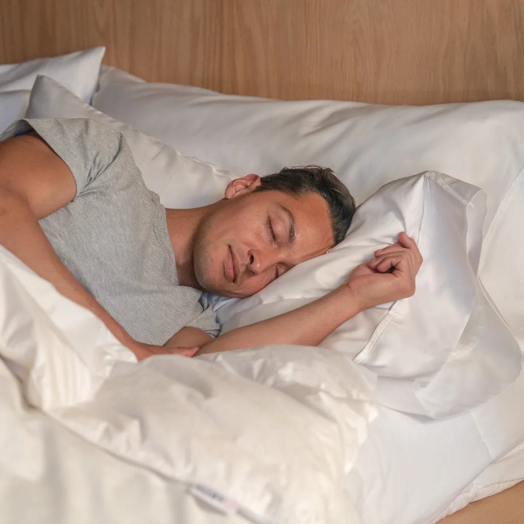 A person sleeping on white pillows against a wood headboard